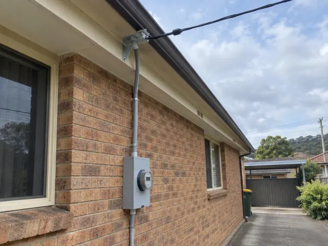 Overhead service cable and point-of-attachment bracket on a brick house exterior in Elermore Vale
